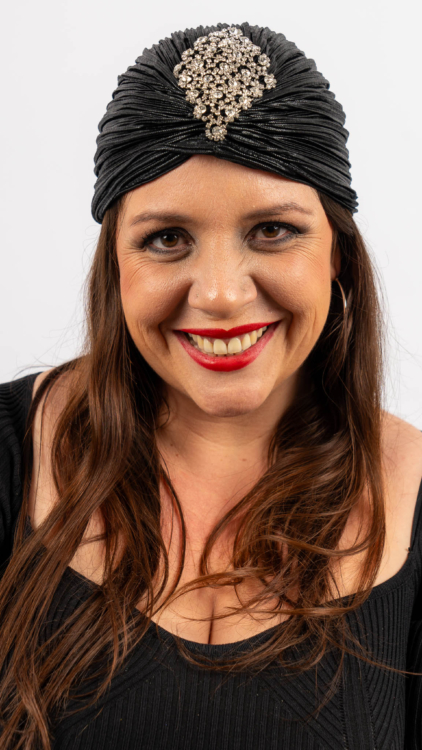 Femme souriante dans une tenue noire portant un foulard orné de bijoux, sur fond blanc. Mode Grande taille