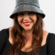 Femme avec un chapeau à motifs et du rouge à lèvres rouge, souriant sur un fond blanc uni. Mode Grande taille