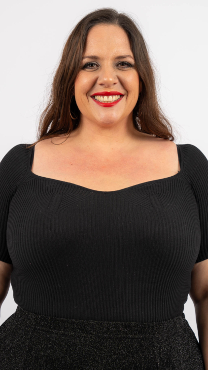 Femme souriante dans un haut noir sur un fond blanc uni. Mode Grande taille