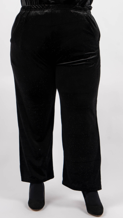 Pantalon en velours noir aux reflets subtils, porté avec des bottines noires sur un fond uni. Mode Grande taille