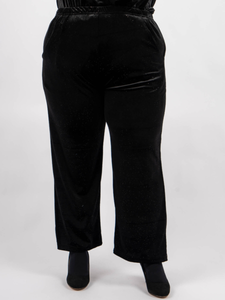 Pantalon en velours noir aux reflets subtils, porté avec des bottines noires sur un fond uni. Mode Grande taille