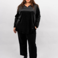 Femme souriante dans une tenue en velours noir posant sur un fond blanc. Mode Grande taille