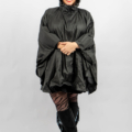 Personne portant un poncho de pluie noir souriant, portant des leggings à motifs et des bottes noires à franges. Mode Grande taille