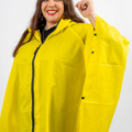 Une femme souriante, portant un poncho de pluie jaune vif avec une capuche, sur un fond blanc uni. Mode Grande taille