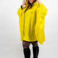 Une personne portant un imperméable jaune vif, des bottes noires jusqu'aux genoux et des leggings à motifs, souriant à la caméra. Mode Grande taille