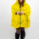 Personne portant un imperméable jaune vif, des bottes noires et des collants à motifs, souriant sur un fond uni. Mode Grande taille