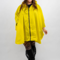 Une femme souriante vêtue d'un imperméable jaune et de bottes noires se tient debout sur un fond blanc. Mode Grande taille