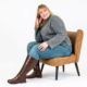 Personne souriante dans un chandail gris et un jean, assise sur une chaise marron, portant les bottes hautes à mollet large Lise 3XL Gabylou. Mode Grande taille