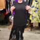 Une personne portant une « Robe sweat avec dentelle » noire se tient debout dans un magasin de vêtements, entourée de vêtements colorés. Mode Grande taille