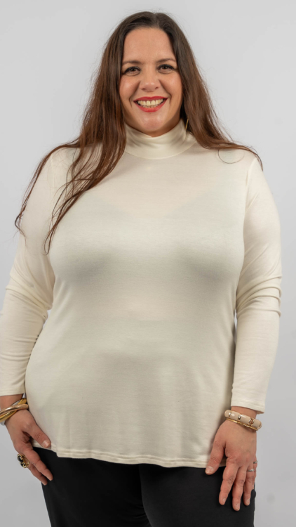 Femme souriante portant un col roulé blanc et un pantalon noir, posant sur un fond uni. Mode Grande taille