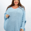 Femme dans un pull bleu clair souriant sur un fond blanc uni. Mode Grande taille