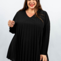 Femme souriante portant un haut plissé noir et un pantalon noir avec de longs cheveux bruns. Mode Grande taille