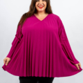 Personne portant un haut fluide et plissé magenta et un pantalon noir, souriant sur un fond uni. Mode Grande taille