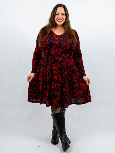 Femme en robe noire à motif floral rouge, souriante, debout sur un fond uni, portant des bottes noires. Mode Grande taille