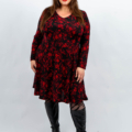 Femme souriante dans une robe fleurie rouge et des bottes noires jusqu'aux genoux debout sur un fond blanc. Mode Grande taille