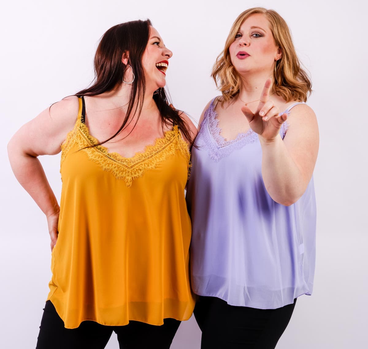 Deux femmes en hauts jaune et violet riant et gesticulant sur un fond blanc. Mode Grande taille