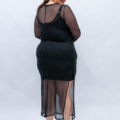 Femme vêtue d'une robe à pois en maille noire, tournée vers l'arrière et souriante, se tient debout sur un fond gris clair. Mode Grande taille