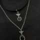 Le « Collier ras de cou anges » présente deux colliers en argent avec des pendentifs sur le thème des anges ; l'un comprend une pierre noire, le tout présenté sur un fond en tissu sombre. Mode Grande taille