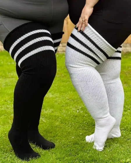 Gros plan de deux personnes portant des Chaussettes hautes jusqu'aux cuisses à rayures noires et blanches, debout sur l'herbe. Mode Grande taille