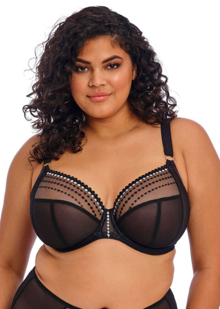 Une personne aux cheveux bouclés portant le soutien-gorge plongeant Elomi Matilda en noir transparent avec des détails en perles, regardant la caméra. Mode Grande taille