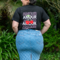 Une personne portant une chemise noire « AMOUR » et une jupe en jean se tient dans un jardin, le dos tourné. Mode Grande taille