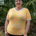 Une personne portant une chemise jaune à imprimé léopard sourit à l'extérieur, debout devant des feuilles de palmier vertes. Mode Grande taille