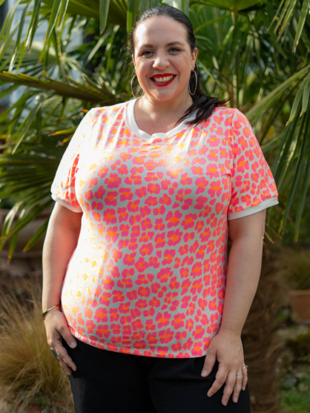 Une personne souriante vêtue d'une chemise à motifs lumineux se tient devant des feuilles de palmier. Mode Grande taille