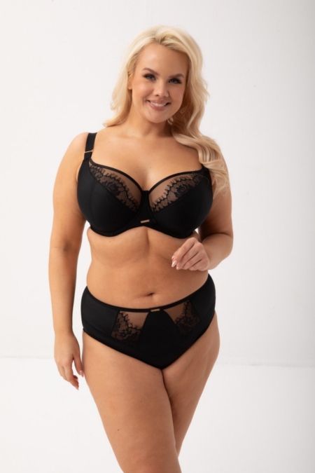 Une femme aux longs cheveux blonds pose pour le Soutien gorge Evia noir, une pièce de lingerie en dentelle noire, debout et souriante dans un studio lumineux. Mode Grande taille