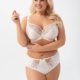 Une femme souriante portant le Soutien gorge Evia noir pose sur un fond blanc uni. Mode Grande taille