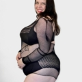 Une femme souriante pose avec assurance dans le Body résille dos ouvert avec motif sur un fond blanc uni. Mode Grande taille
