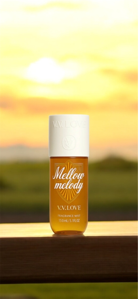 Une bouteille de brume de parfum V.V. Love Mellow Melody sur une surface en bois avec un arrière-plan de coucher de soleil. Mode Grande taille