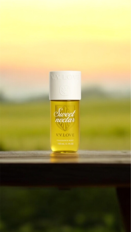 Une bouteille jaune étiquetée "Sweet nectar V.V. LOVE" est posée sur une surface en bois avec un arrière-plan flou de coucher de soleil. Mode Grande taille