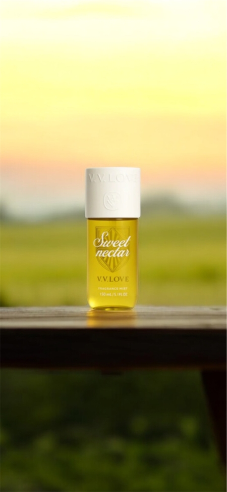 Une bouteille jaune étiquetée "Sweet nectar V.V. LOVE" est posée sur une surface en bois avec un arrière-plan flou de coucher de soleil. Mode Grande taille