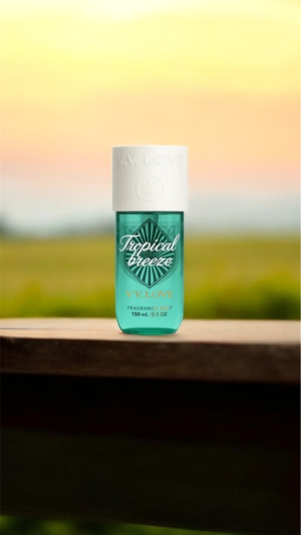 Un flacon de parfum turquoise étiqueté "Fruital Breeze" est posé sur un rebord en bois avec un arrière-plan flou de coucher de soleil. Mode Grande taille