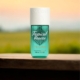 Un flacon de parfum turquoise étiqueté "Fruital Breeze" est posé sur un rebord en bois avec un arrière-plan flou de coucher de soleil. Mode Grande taille