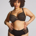 Une femme pose avec assurance dans le soutien-gorge bonnet intégral Sophia, un ensemble de dentelle noire assorti, sur un fond neutre. Mode Grande taille