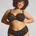 Une femme souriante aux cheveux bouclés pose avec assurance en portant le soutien-gorge emboîtant Sophia en dentelle noire et la culotte assortie. Mode Grande taille