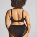 Une femme aux cheveux bouclés présente le soutien-gorge Sophia full-cup en dentelle noire de dos, sur un fond neutre. Mode Grande taille