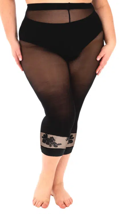 Une femme porte le modèle "Legging collants avec dentelle florale", un legging noir transparent avec des détails de dentelle florale près du mollet, alors qu'elle se tient pieds nus sur un fond blanc. Mode Grande taille