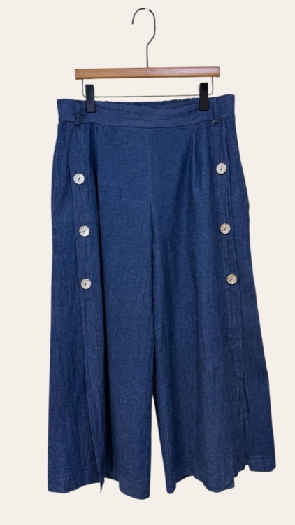La Jupe culotte en denim détail boutons présente un modèle bleu à jambe large avec six boutons blancs, présenté sur un cintre en bois sur fond uni. Mode Grande taille