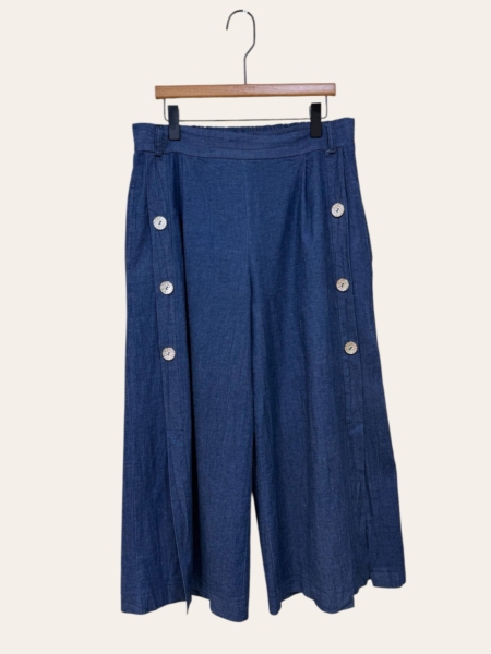 La Jupe culotte en denim détail boutons présente un modèle bleu à jambe large avec six boutons blancs, présenté sur un cintre en bois sur fond uni. Mode Grande taille