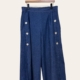 La Jupe culotte en denim détail boutons présente un modèle bleu à jambe large avec six boutons blancs, présenté sur un cintre en bois sur fond uni. Mode Grande taille