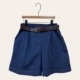 Jupe culotte en denim détail boutons, présentée sur un cintre en bois contre un fond uni. Mode Grande taille