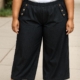 Personne portant le pantalon jambes larges avec boutons décoratifs, un t-shirt blanc et des baskets blanches, debout à l'extérieur. Mode Grande taille