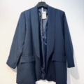Blazer ouvert en bleu marine avec revers et poches, présenté sur un cintre noir contre un mur blanc. Mode Grande taille