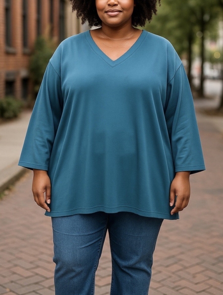 Une personne portant le maillot Tunique sweat col V en et un jean se tient sur un trottoir en briques dans un environnement urbain. Mode Grande taille