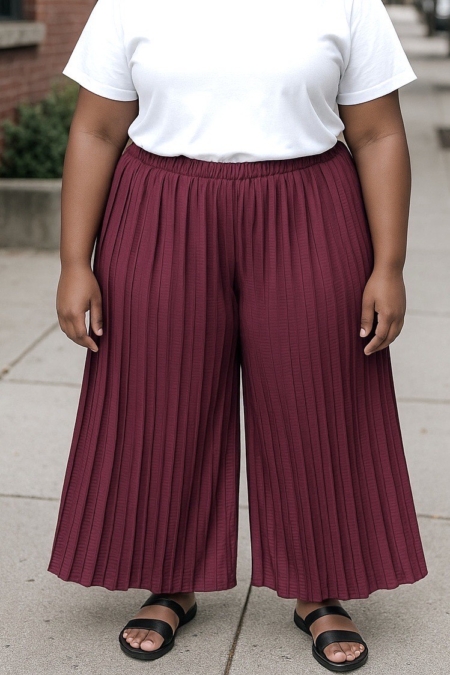 Personne portant un t-shirt blanc, un pantalon jupe culotte plissé de couleur bordeaux et des sandales noires, debout sur un trottoir. Mode Grande taille