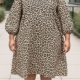 Personne portant la "Robe fluide manches bouffantes imprimé animalier", une robe ample à manches longues imprimée animalier, debout en plein air sur un chemin pavé. Mode Grande taille