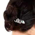 Les cheveux noirs d'une femme sont coiffés en chignon et ornés de l'Épingle à Cheveux Médusa, une épingle à cheveux en argent en forme de serpent, ornée d'une pierre précieuse verte. Mode Grande taille