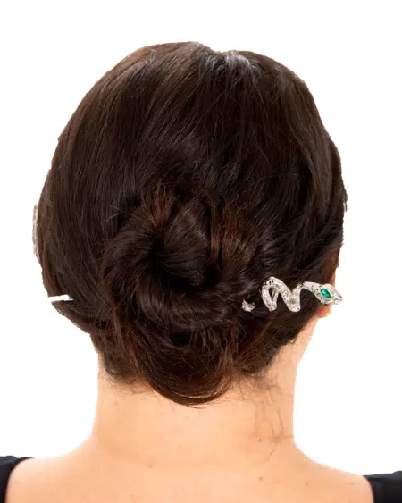 Femme aux cheveux noirs en chignon, ornée de l'Épingle à Cheveux Médusa, une épingle à cheveux en argent en forme de serpent aux yeux verts. Mode Grande taille